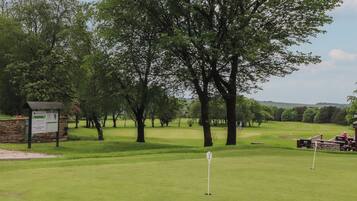 A golf course with a signboard, trees, and a well-maintained green.
