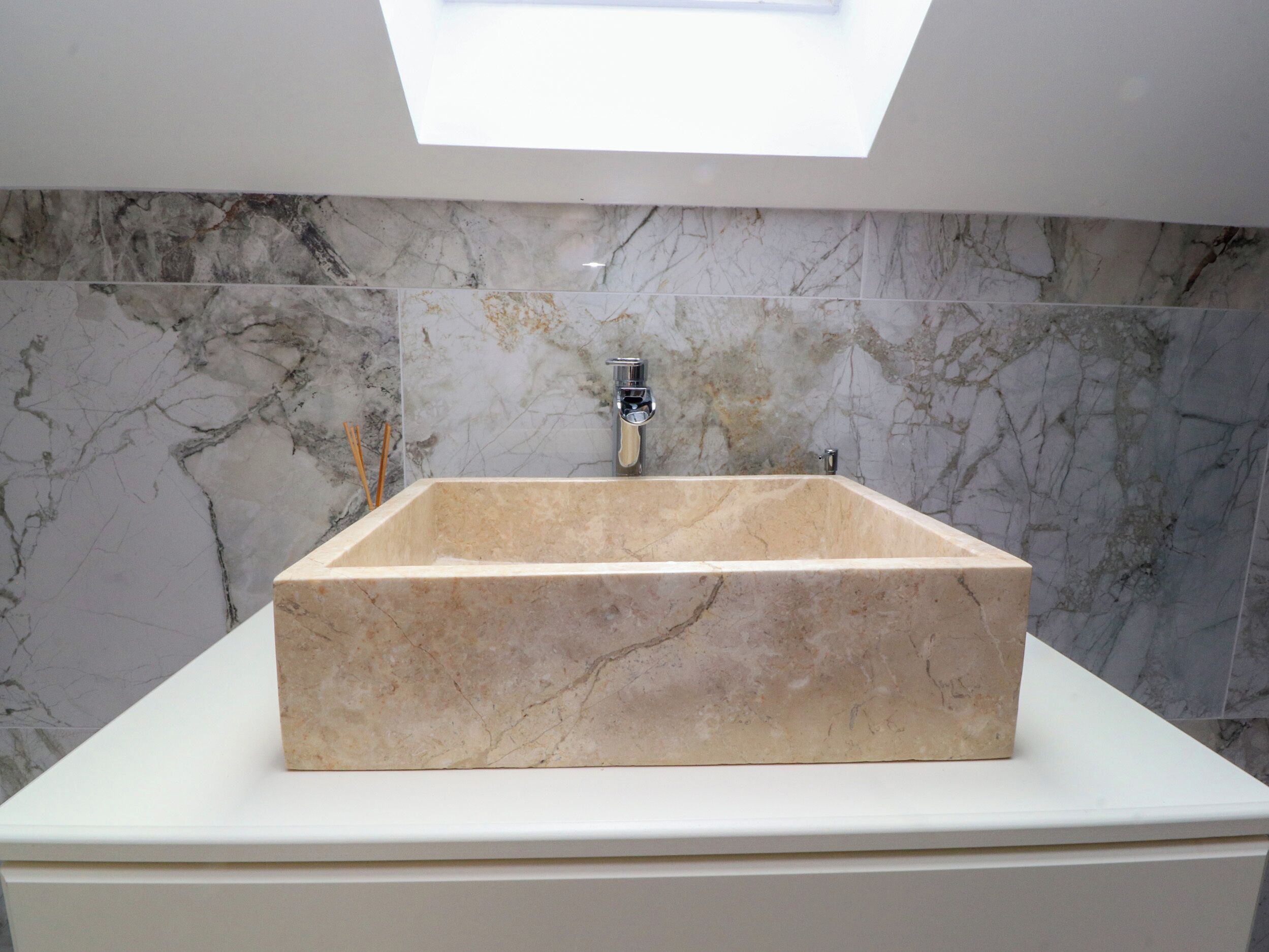 Un baño con un lavamanos de mármol rectangular, un grifo moderno y un tragaluz.