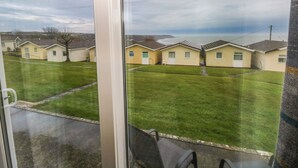 A row of single-story houses with a grassy yard in front, a clear sky, and a body of water in the background. - Chalet 22 (Swansea)