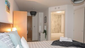 Ett hotellrum med en säng, en sänglampa, en dörr som leder till ett badrum och en väggmonterad lampa.