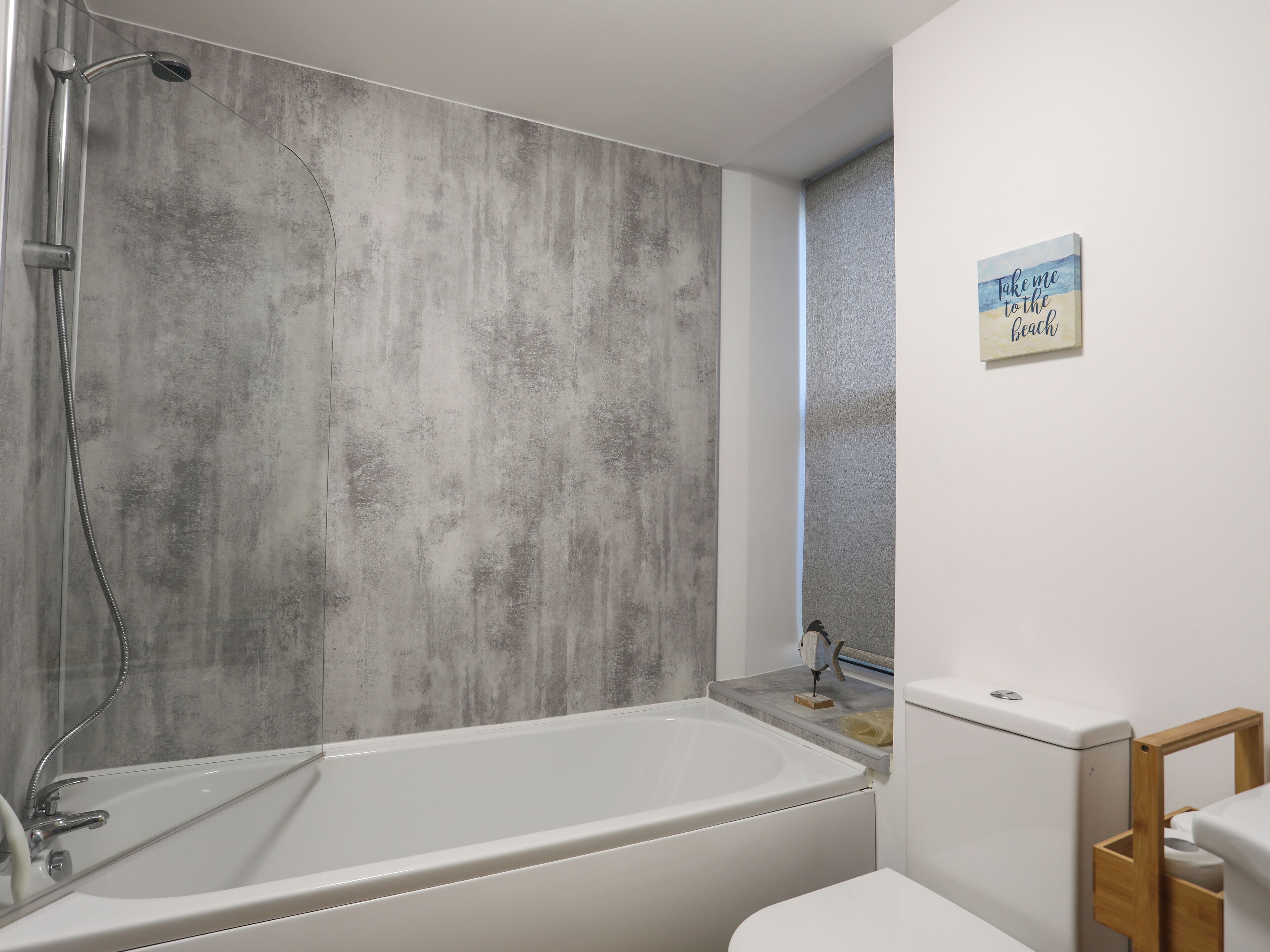 Un baño moderno con bañera, ducha e inodoro. Hay un perchero y un letrero en la pared.