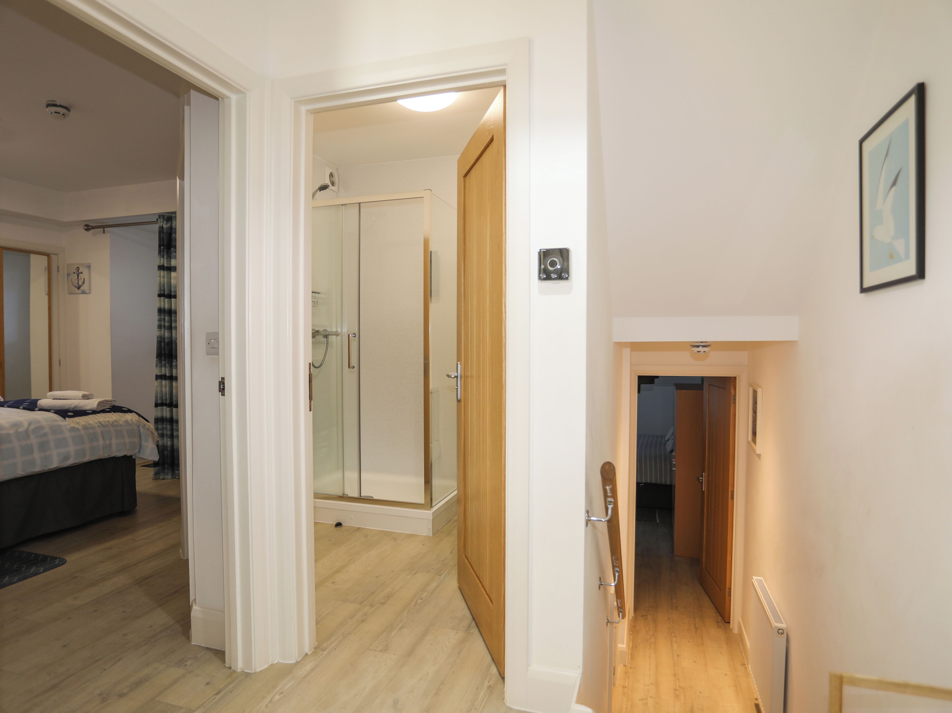 A bedroom with a bed, a bathroom with a shower, and a hallway leading to another room.