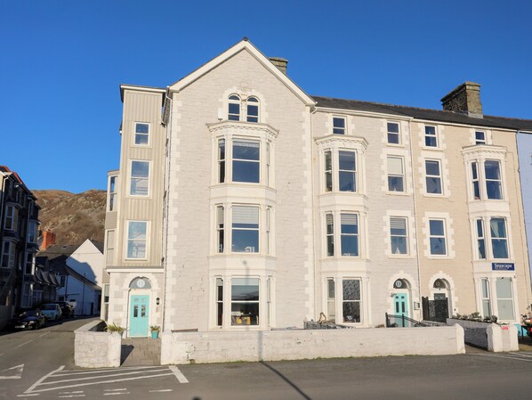 A multi-story building with a classic architectural style, featuring a prominent entrance with a blue door and a small porch area. - Sandcastles (Barmouth)