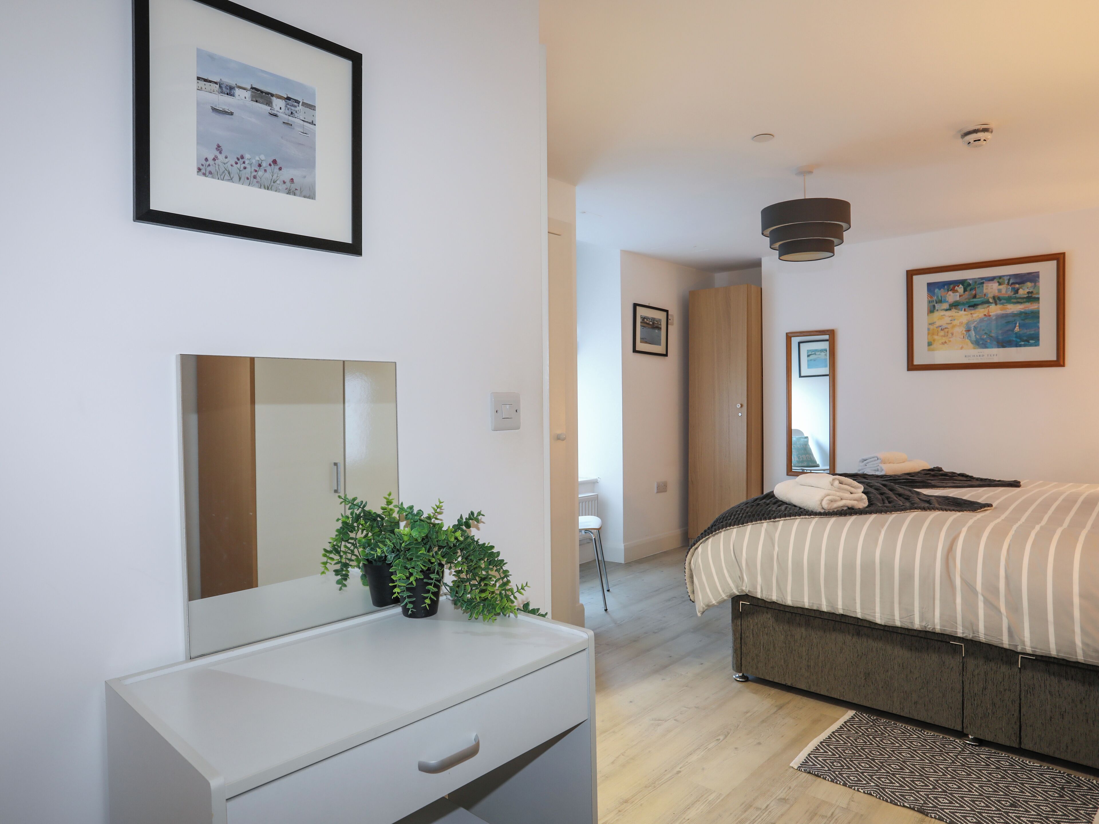 Ein modernes Schlafzimmer mit Bett, Nachttisch, Spiegel und einer Topfpflanze.