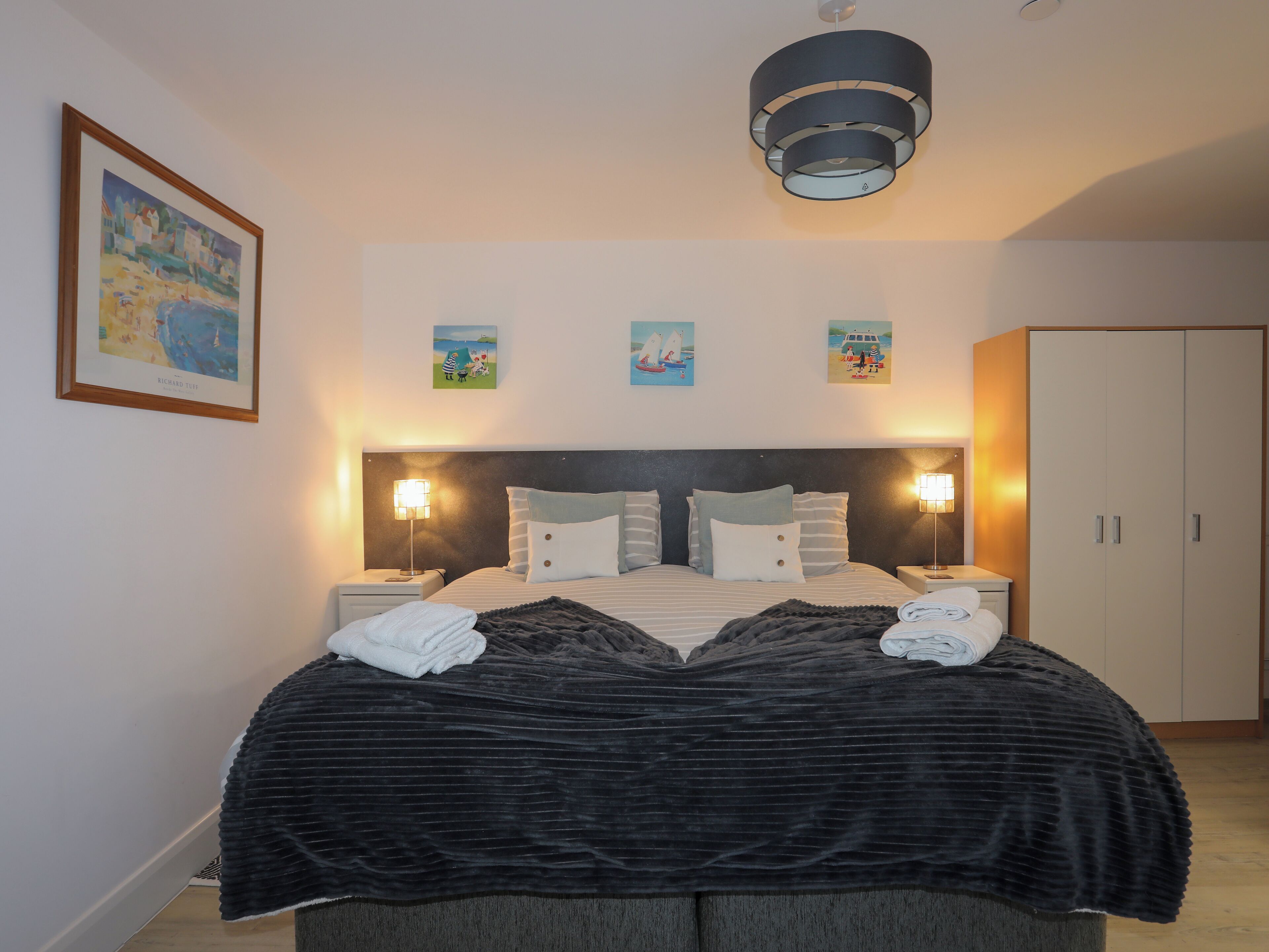 A neatly made bed with a dark bedspread and two white towels, flanked by two bedside lamps.