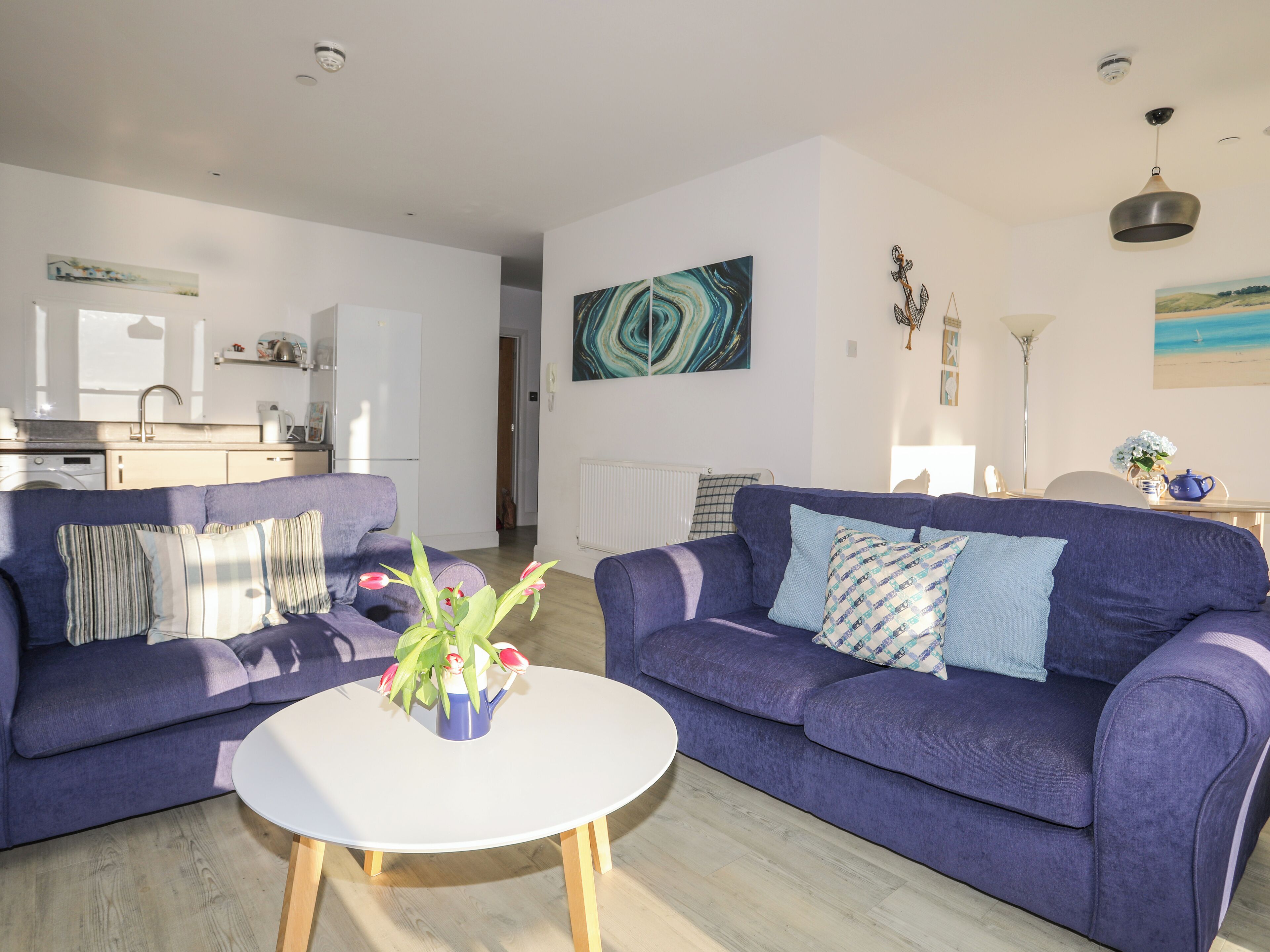 Un salon moderne avec un canapé violet, une table basse blanche et un coin cuisine à l’arrière-plan.
