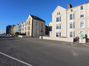 A street with multi-story buildings, including a corner building with a bay window and a building with a blue door. - Sandcastles (Barmouth)