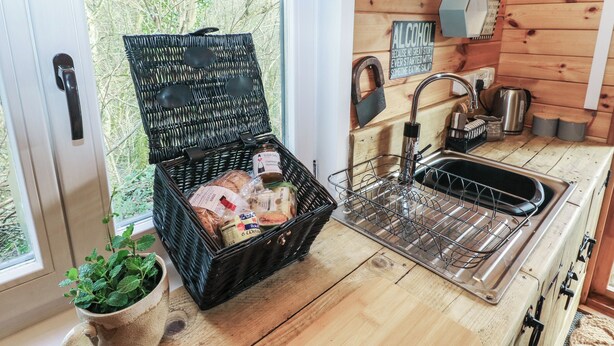 Une cuisine rustique avec un panier en osier contenant du pain et une bouteille de vin, un évier et une fenêtre donnant sur la verdure.
