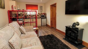 A living room with a sofa, a black rug, a TV, and a wood-burning stove. - Stable Cottage (Newcastle-upon-Tyne)