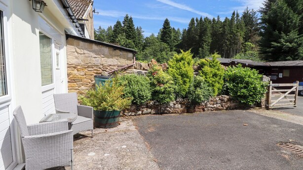 A stone building with a tiled roof, a gravel driveway, and a wooden gate. - Stable Cottage (Newcastle-upon-Tyne)