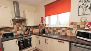 A modern kitchen with white cabinets, a stainless steel range hood, a microwave, and a dishwasher. - Stable Cottage (Newcastle-upon-Tyne)