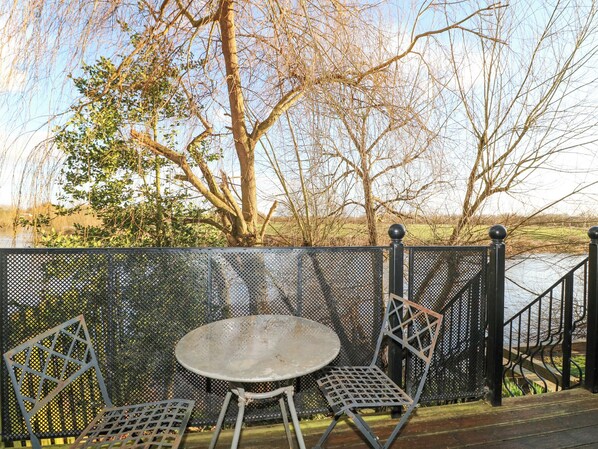 A metal table and two chairs on a deck with a view of a tree and a body of water. - River Cottage (Derby)