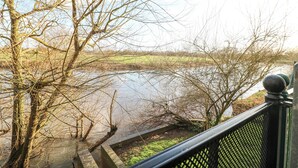 A riverside view from a balcony with bare trees and a brick pathway leading to the water. - River Cottage (Derby)