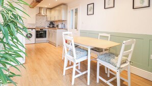 A kitchen with wooden cabinets, a dining table with chairs, and a large plant. - River Cottage (Derby)