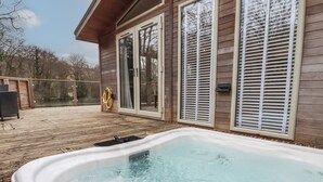 Un bain à remous sur une terrasse en bois, doté d’une porte vitrée et de volets, donnant sur une étendue d’eau.