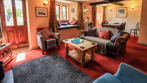 A cozy living room with a fireplace, a sofa, a chair, and a dining area. - Tethera Cottage (Penrith)