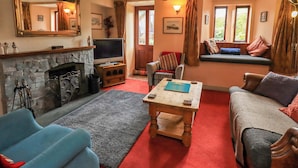 A living room with a stone fireplace, a television, a sofa, and a window seat. - Tethera Cottage (Penrith)