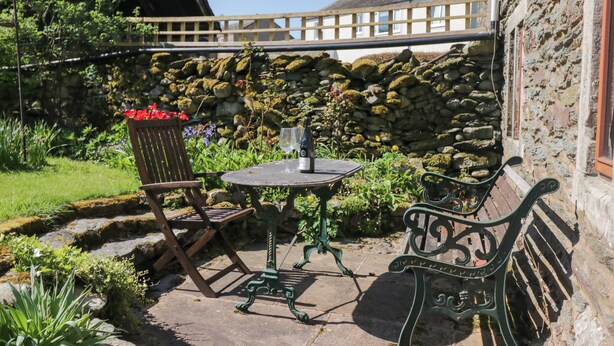A stone wall, a wooden fence, and a table with chairs in a garden area. - Tethera Cottage (Penrith)