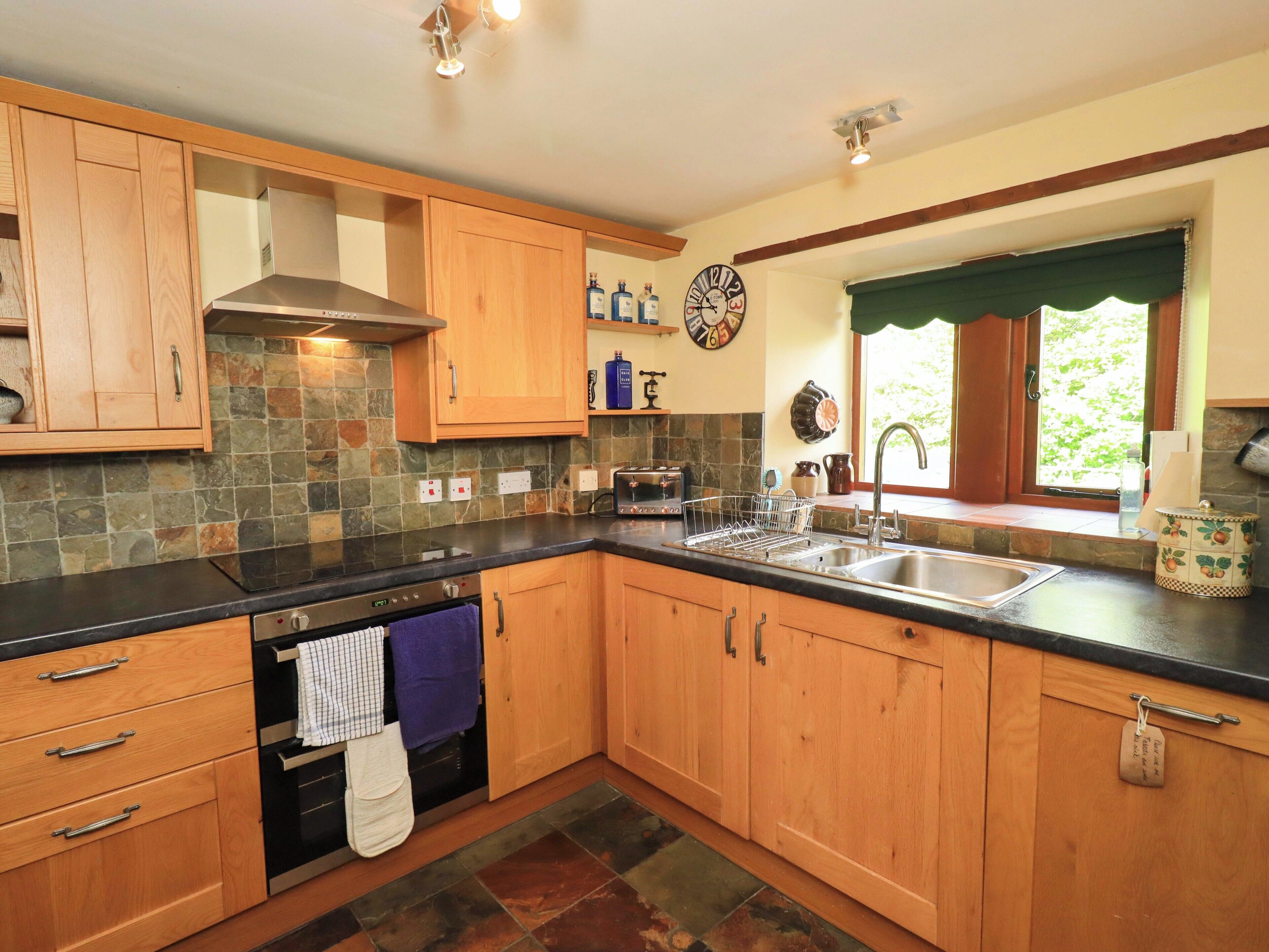 A kitchen with wooden cabinets, a black countertop, a stainless steel sink, and a window with a view of greenery.