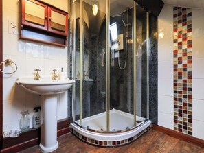 Un baño con ducha de vidrio, lavamanos pedestal y pared de azulejos con diseño de mosaico.