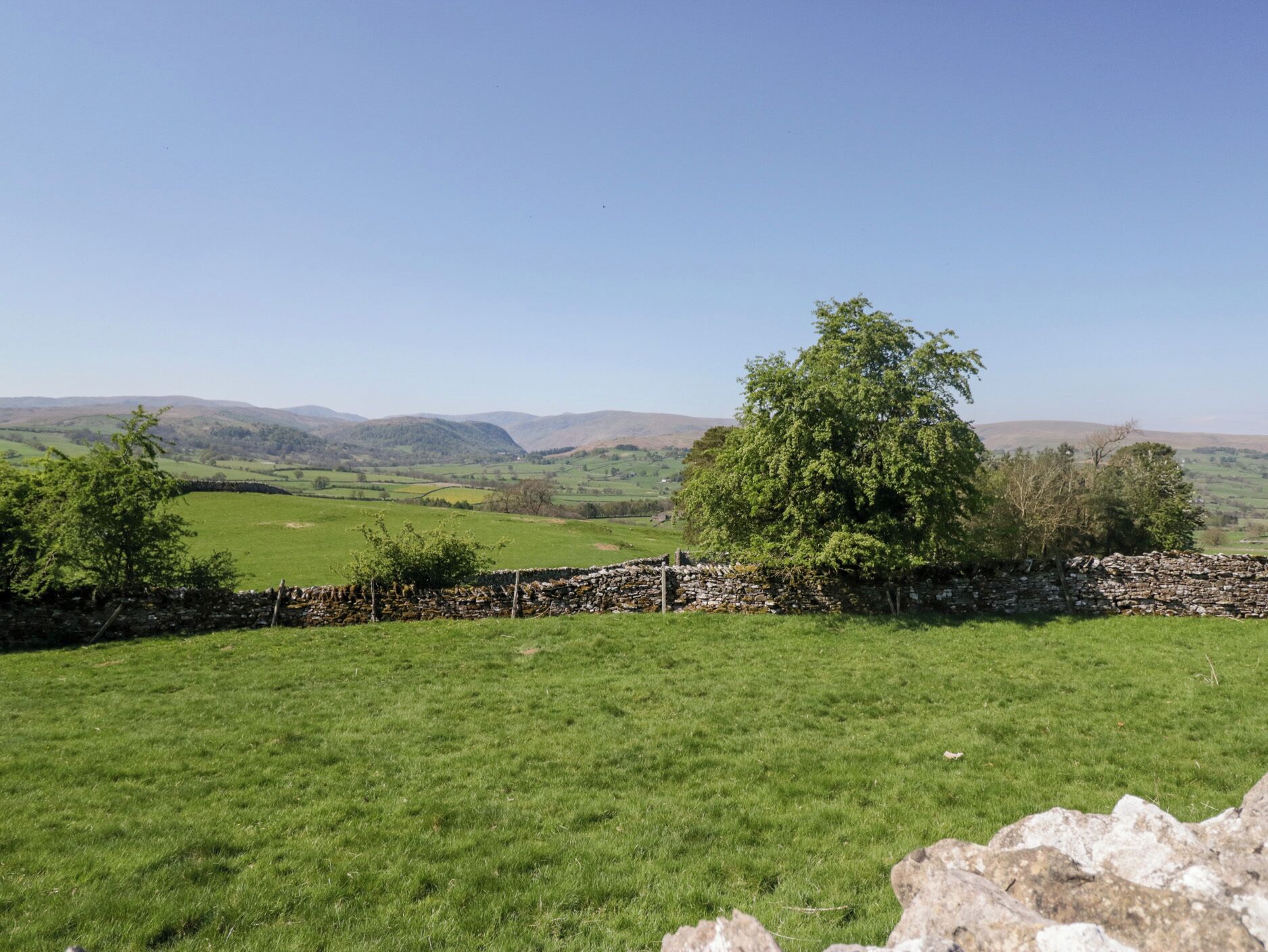 Ländliche Landschaft mit einer Steinmauer, grünen Feldern und fernen Hügeln.