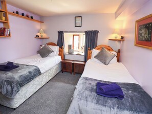 A hotel room with two beds, a desk with a laptop, a mirror, and shelves with books and decorative items. - Tethera Cottage (Penrith)