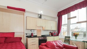 A compact room with a kitchenette, a bed, a red leather sofa, and a window with a view of buildings. - 9 Old City Chambers (Bristol)