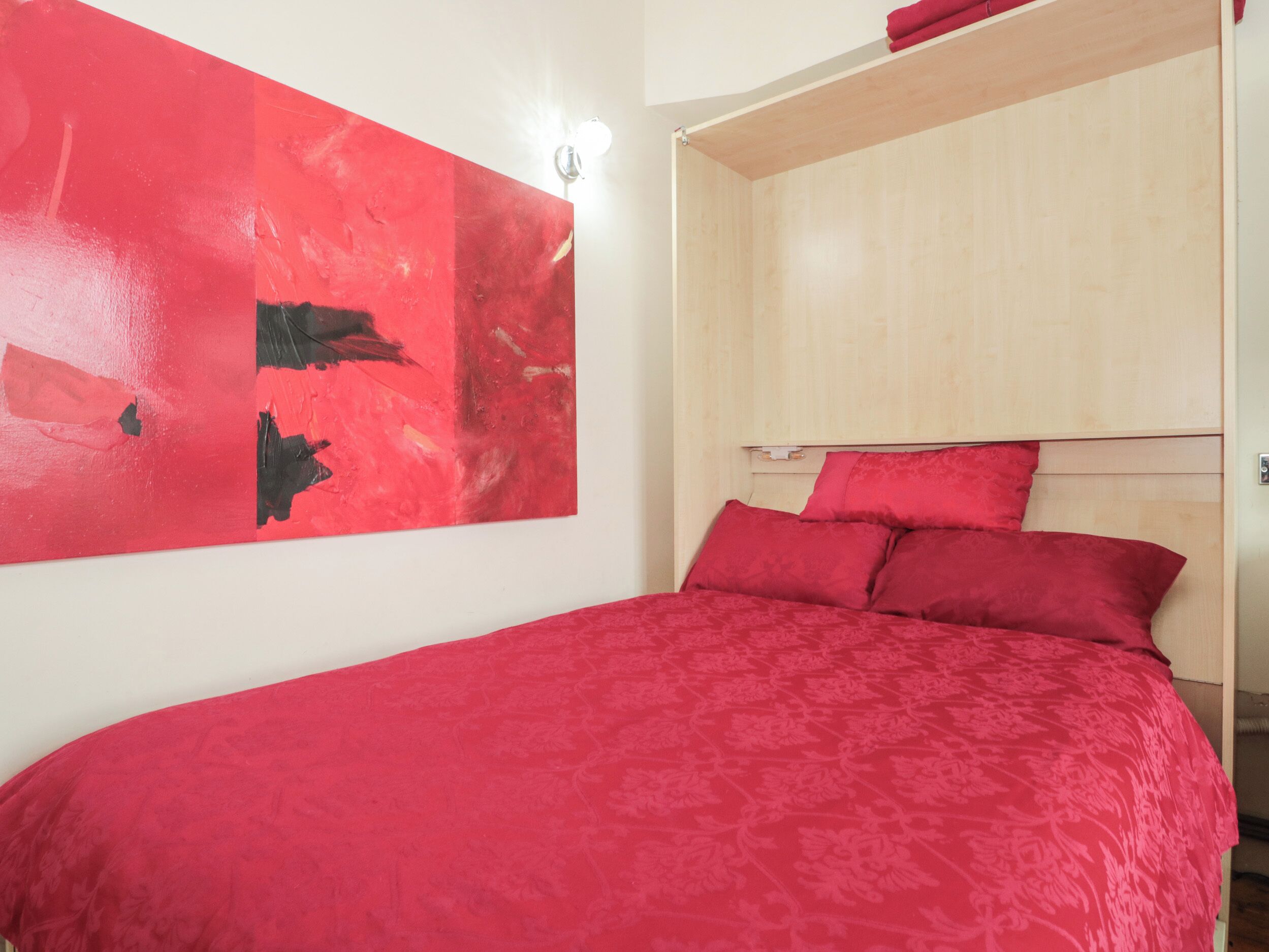 A bedroom with a bed, a red abstract painting, and a wooden headboard.