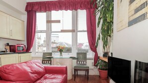 A cozy living room with a red leather sofa, a dining table with chairs, a red curtain, a potted plant, and a flat-screen TV. - 9 Old City Chambers (Bristol)
