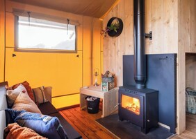 Una habitación acogedora con detalles de madera, un sofá con cojines, una mesita con una lámpara y un estufa de leña.