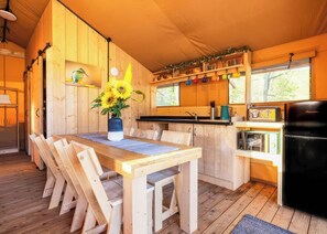 Una cabaña de madera con comedor, cocina y un amplio ventanal.