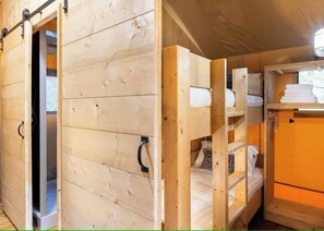Una cabaña de madera con literas, una pequeña kitchenette y una puerta corredera.