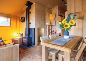 Una cabaña de madera acogedora con chimenea central, una mesa de comedor con bancos y un jarrón de girasoles sobre la mesa.