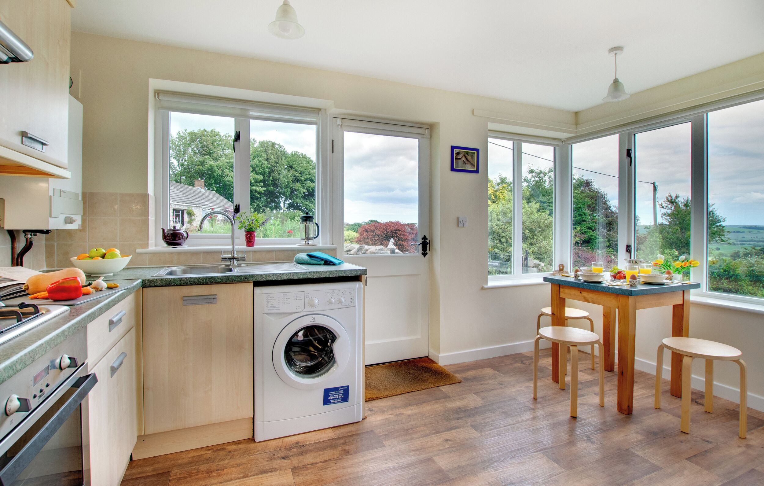 A modern kitchen with a built-in washer, wooden cabinets, and large windows offering a view of the outdoors.