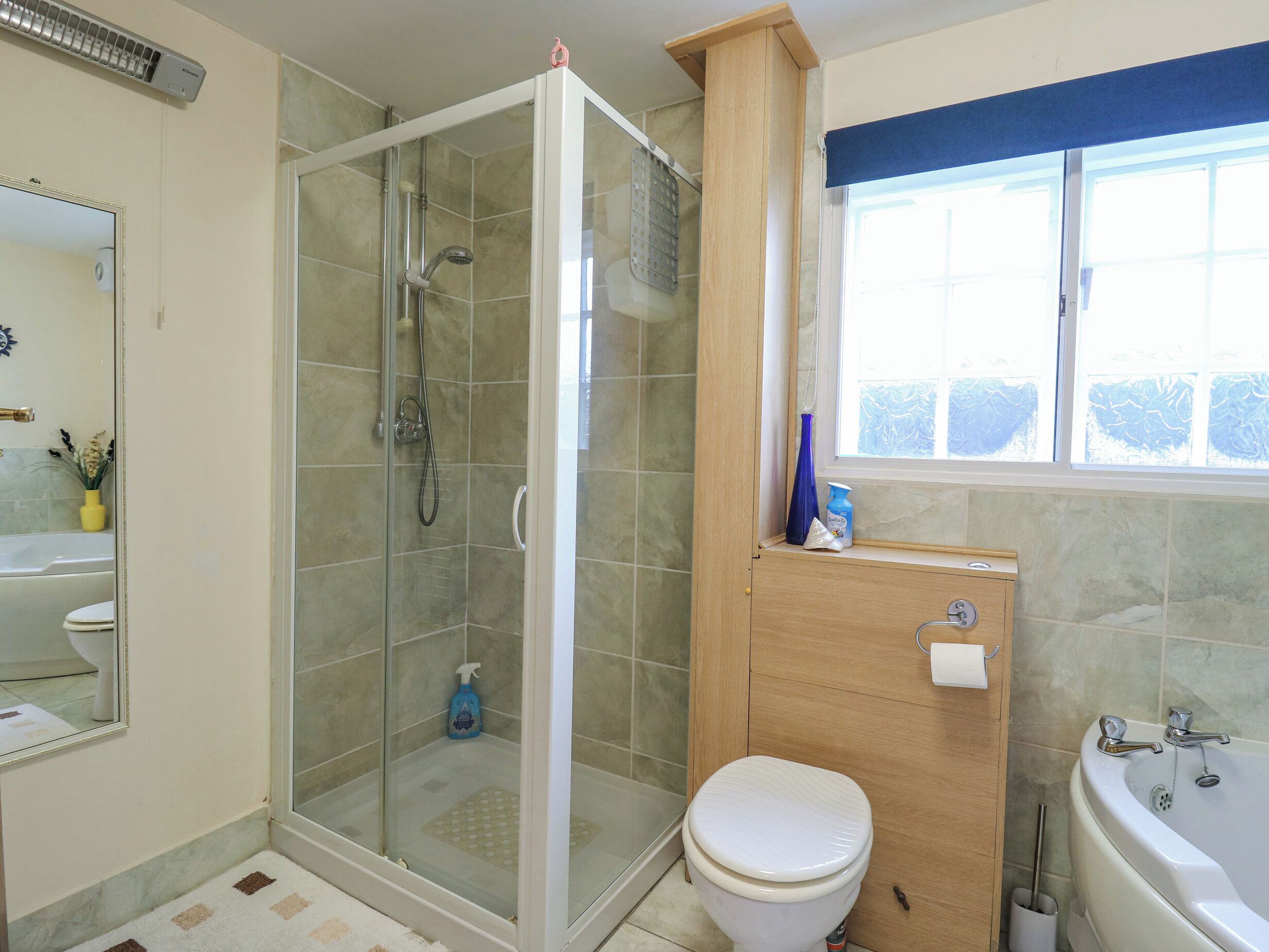 Un bagno con doccia vetrata, un water, un lavandino e una finestra.