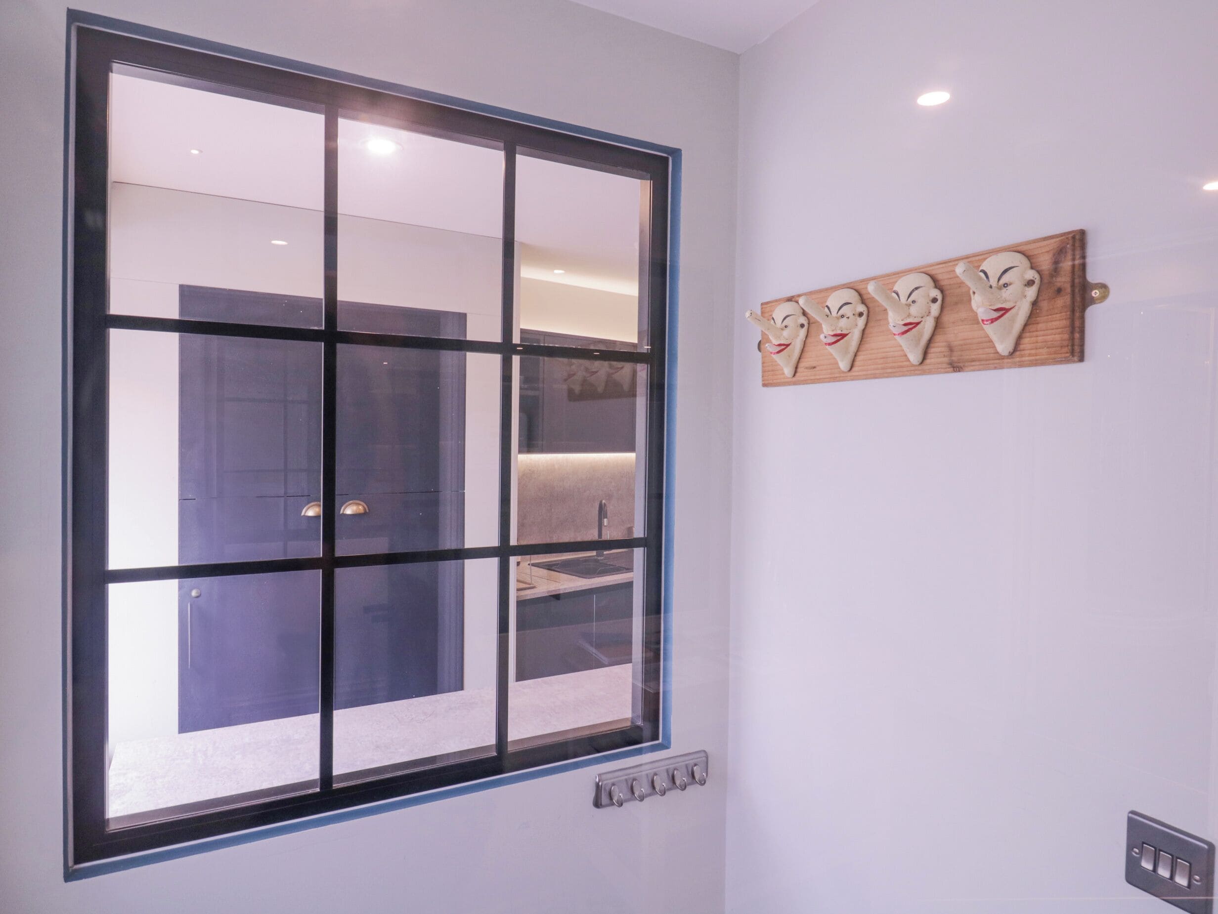 A modern kitchen with a large window, a wall-mounted light fixture, and a decorative wooden piece with animal faces.