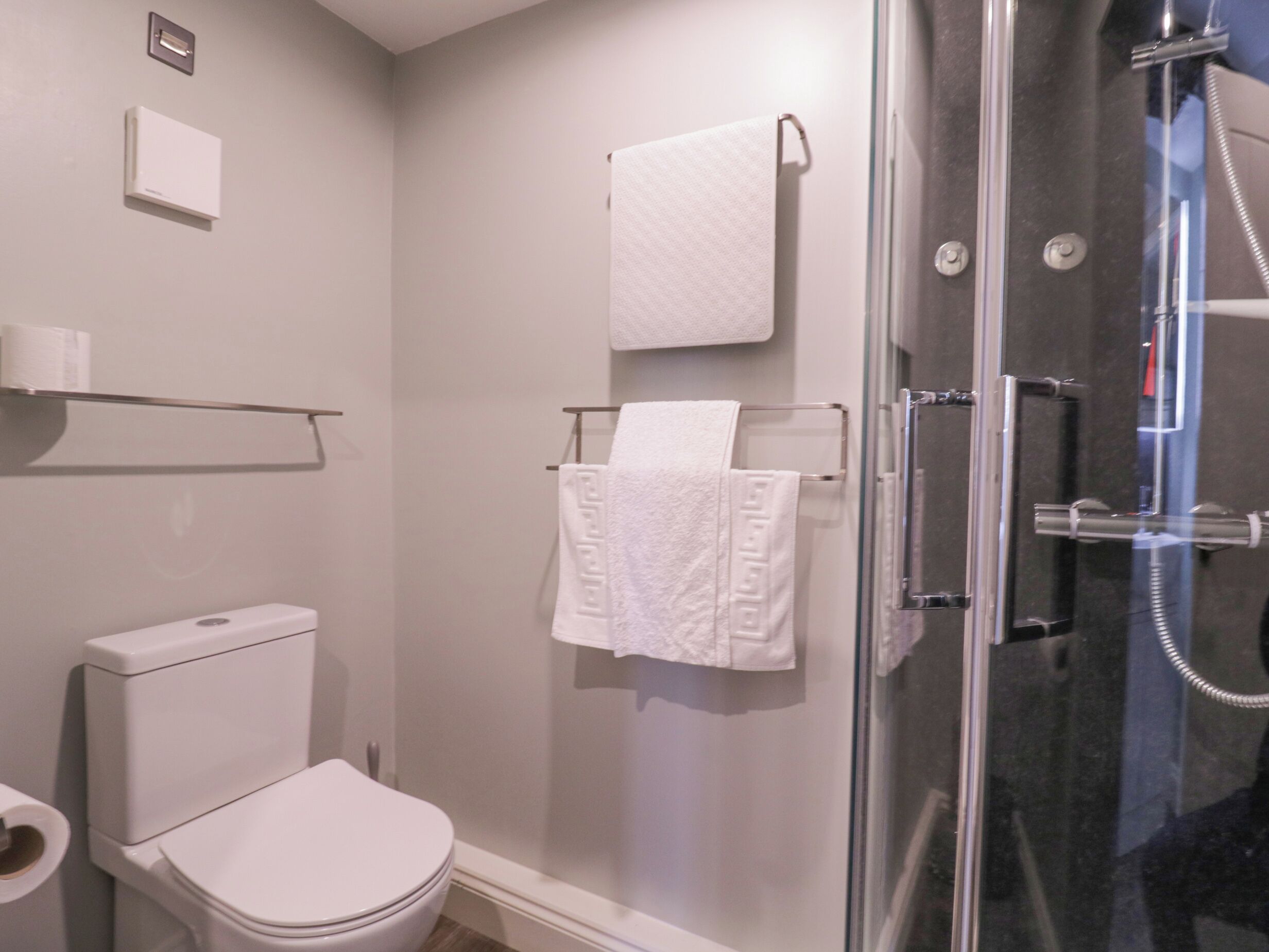 Un baño moderno con inodoro, cabina de ducha de vidrio y toallero con dos toallas blancas.