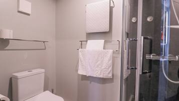 Un baño moderno con inodoro, cabina de ducha de vidrio y toallero con dos toallas blancas.