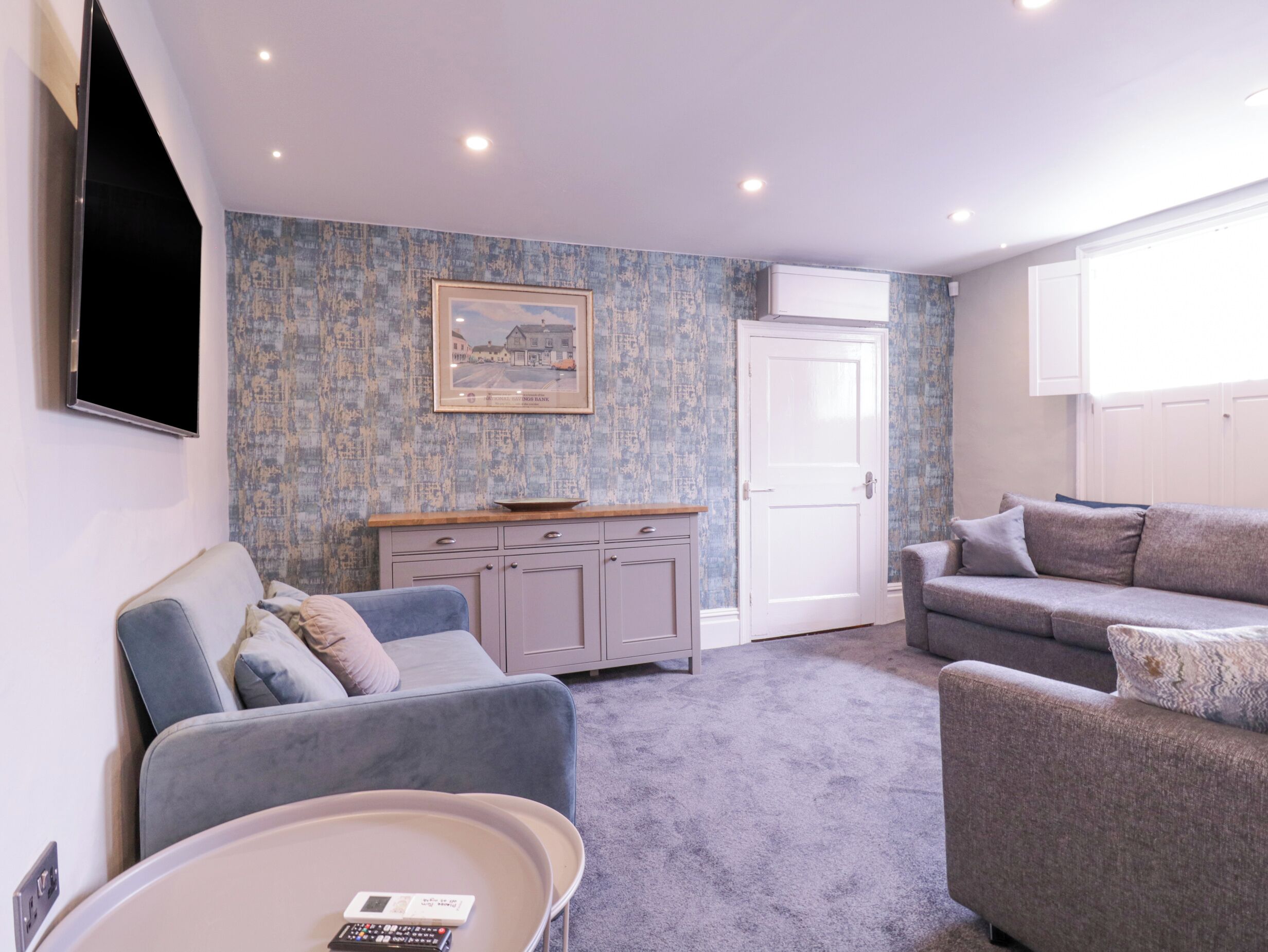 A living room with a grey sofa, a smaller grey armchair, a coffee table, and a cabinet with a picture on the wall.