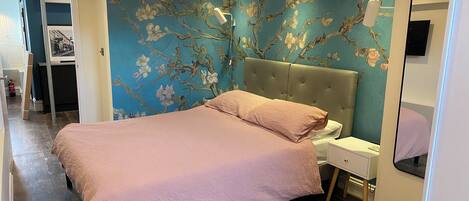 A bedroom with a bed, a nightstand, a mirror, and a wall with floral wallpaper.