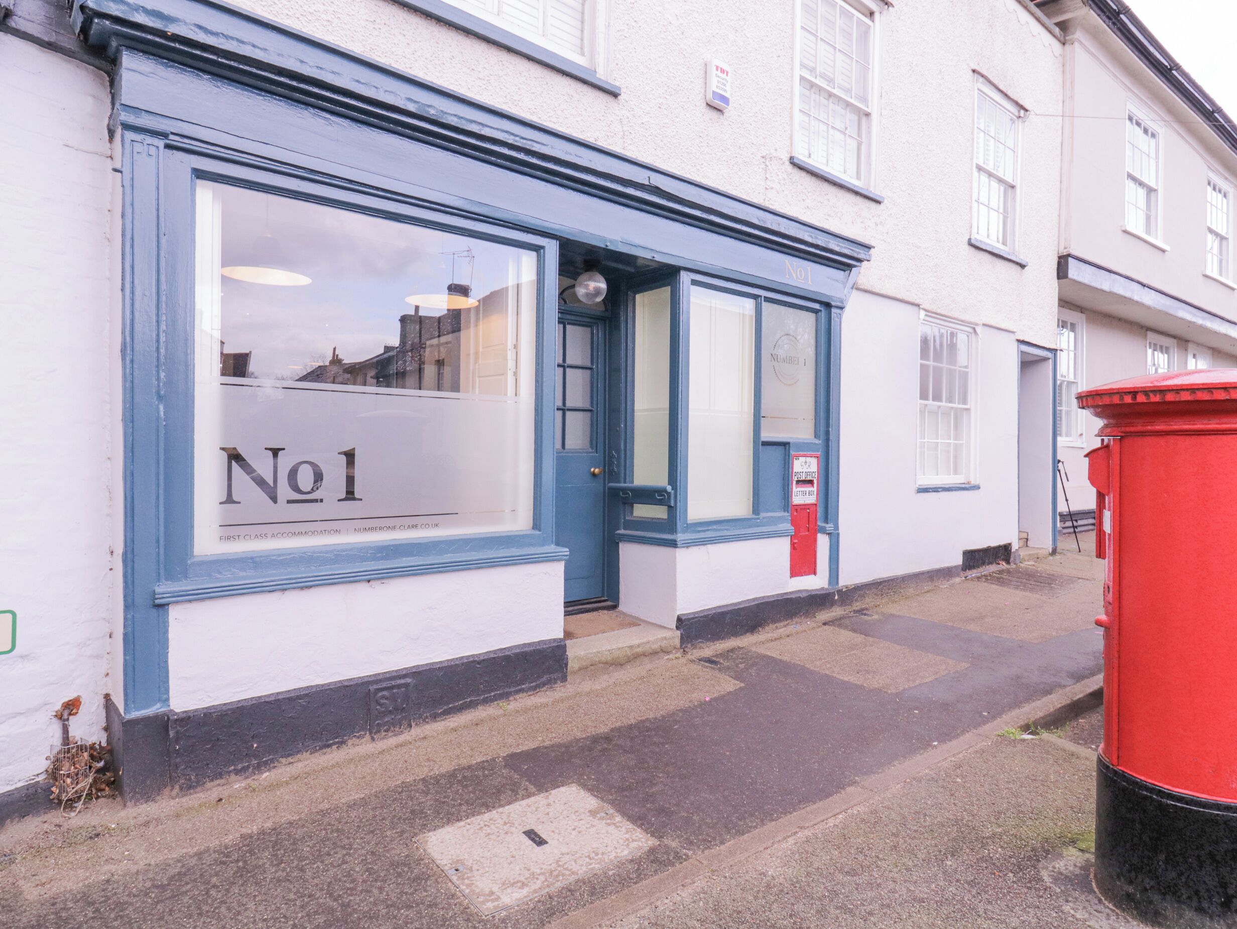 Un bâtiment à la façade bleue et blanche, avec une boîte aux lettres rouge et une enseigne indiquant « N° 1 ».