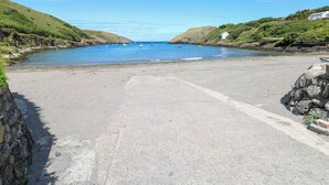 A coastal road leading to a beach with boats in the water and a white building on the right. - Llain Gwynfor (Haverfordwest)