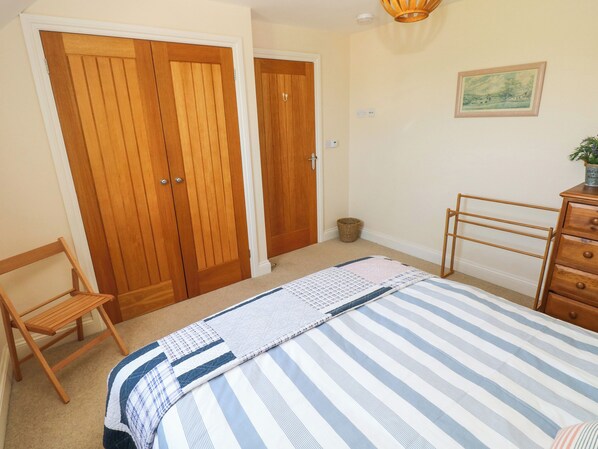 A bedroom with a bed, wooden wardrobe, a chair, a dresser, and a small basket.