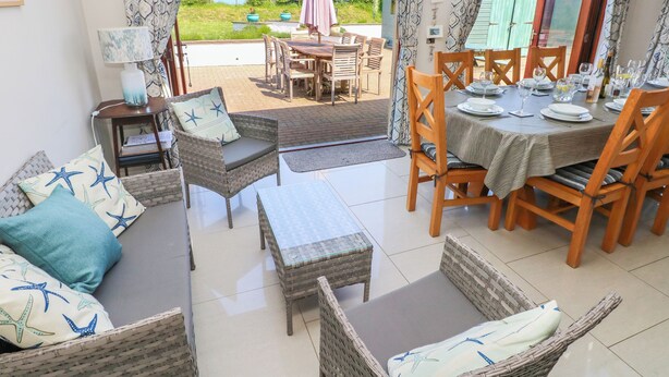 A dining area with wicker furniture, a table set for four, and a view of the outdoors. - Llain Gwynfor (Haverfordwest)
