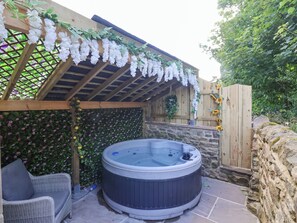 A hot tub in a covered outdoor area with a wooden pergola and decorative flowers. - Waters Edge Lock View (Skipton)