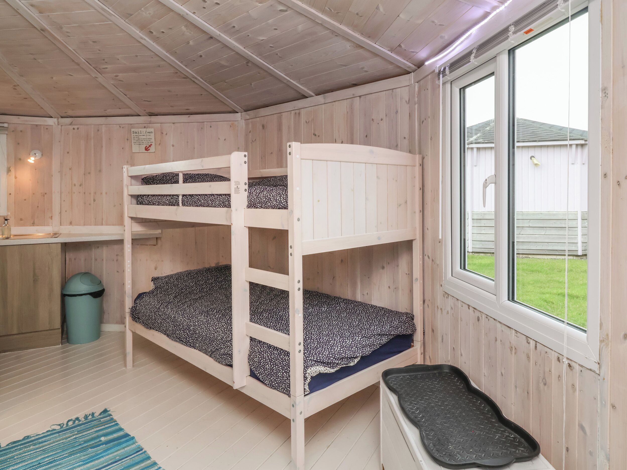 A bunk bed room with a window, a trash bin, and a small shelf.