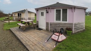 A small, single-story building with a door and windows, a wooden deck, and a picnic table.