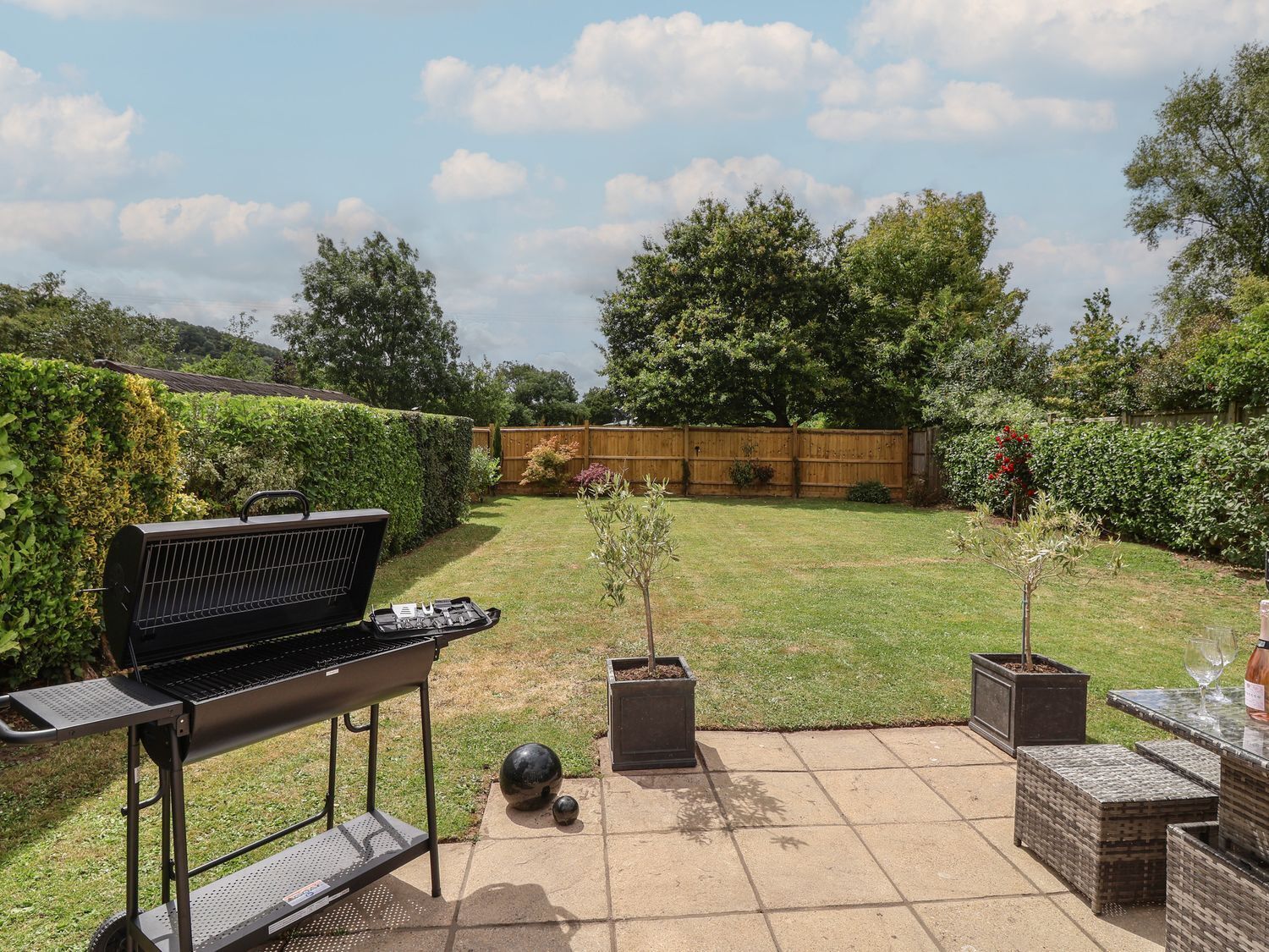 A backyard with a barbecue grill, a small table with a glass, and potted plants.
