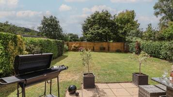 A backyard with a barbecue grill, a small table with a glass, and potted plants.