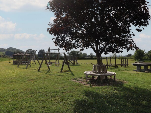 A playground with swings and a picnic table in a grassy field.